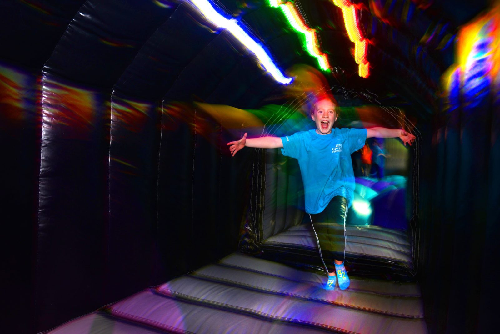 child running through a black tunnel with multi coloured LED lighting above